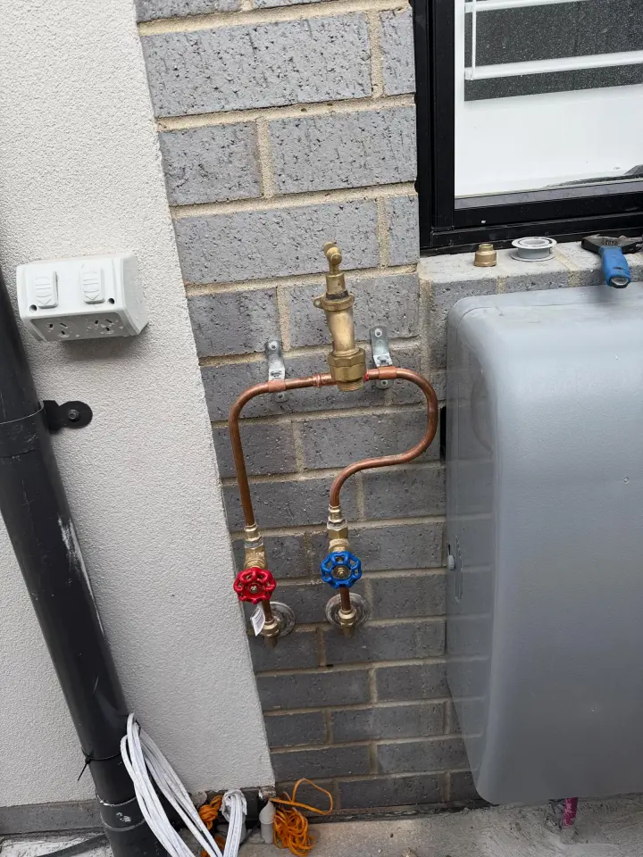 Copper pipework with brass tempering valve and red and blue isolation valves mounted on a brick wall