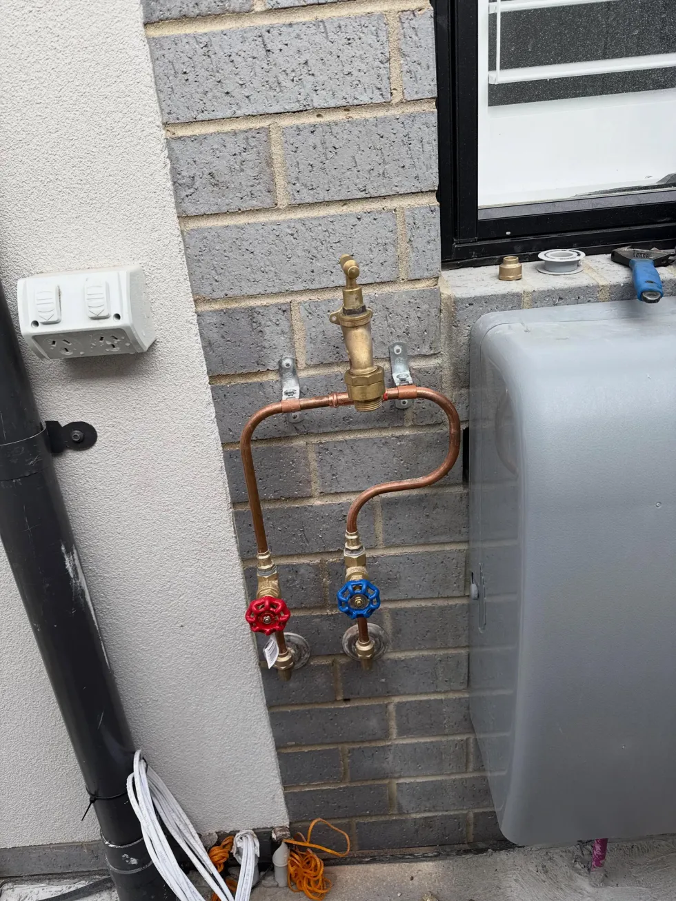 Copper pipework with a brass tempering valve and red and blue isolation valves on a brick wall