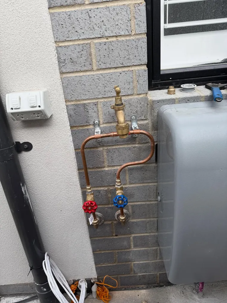 Copper pipework with a brass tempering valve and red and blue isolation valves on a brick wall