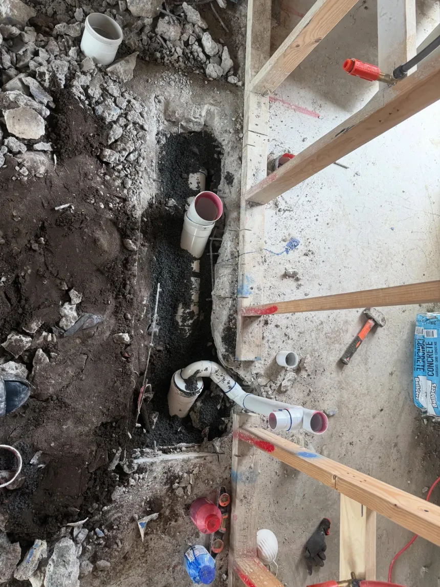 Drainage rough-in inside a house, PVC pipework and junctions bedded in gravel and set to fall before the floor goes down