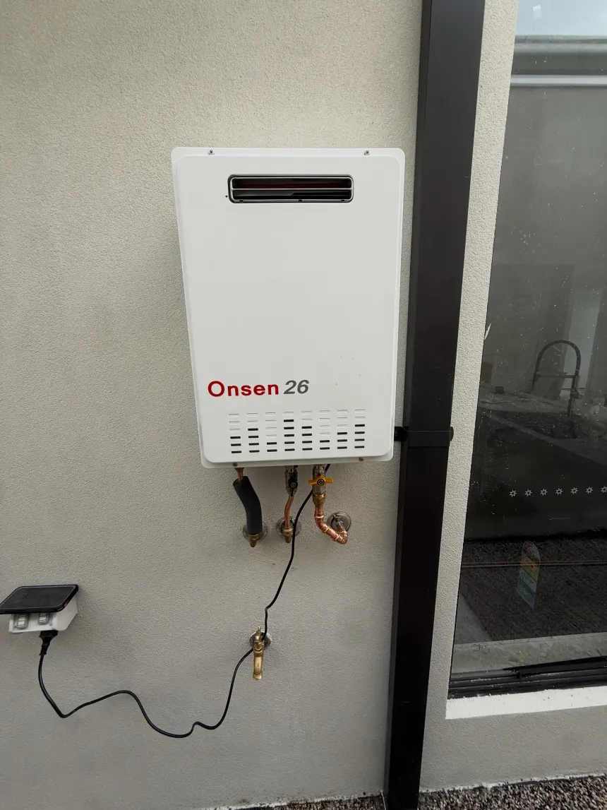 Completed instantaneous hot water unit mounted on a rendered wall with tidy copper and gas connections below it