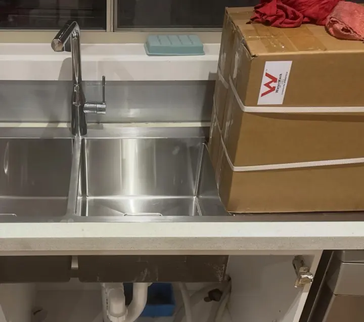 Newly installed stainless steel double kitchen sink and mixer tap with the cabinet open below