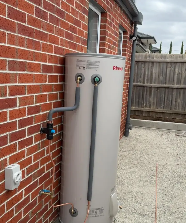 Storage hot water unit installed against a brick wall with insulated copper connections and an isolation valve